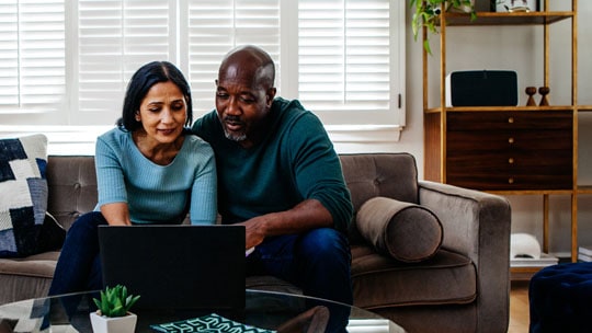 A couple sitting on a sofa looking at an open laptop.